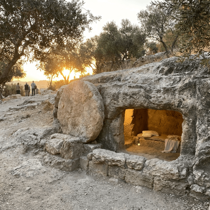 Ancient rock-cut tomb with a large round stone rolled away from the illuminated entrance.